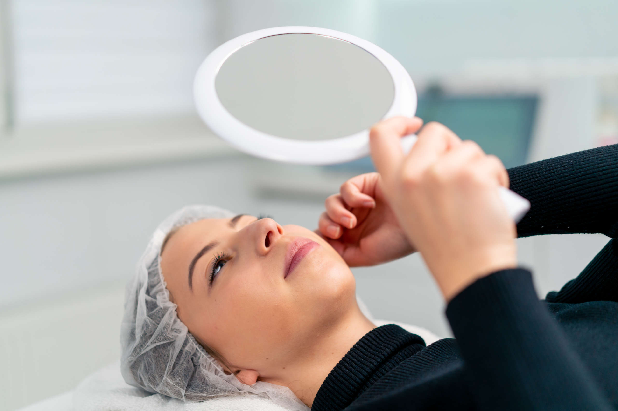 the satisfied face of a female client in a beauty salon looks in the mirror and enjoys the result of cosmetic procedure